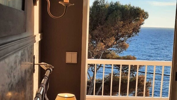 Un balcon avec vue sur la mer et une falaise couverte d’arbres.