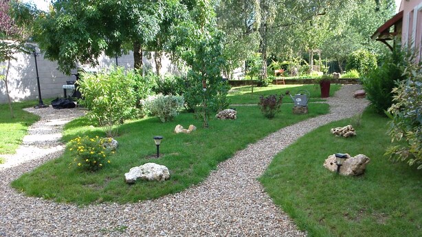 Un sendero en un jardín con grava, rodeado de césped y diversas plantas.