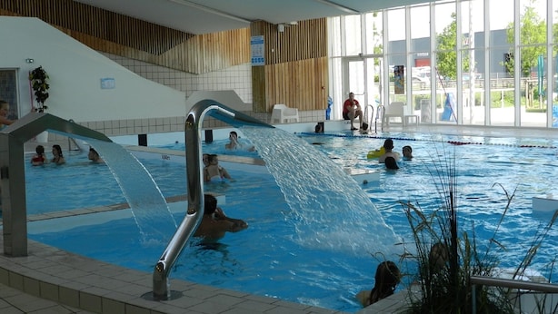 An indoor swimming pool with multiple lanes, a water slide, and a wooden sloped ceiling.