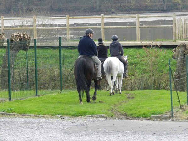 Three people riding horses along a fenced path with a body of water in the background.