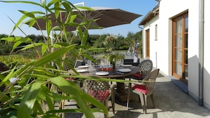 An outdoor patio with a table set for dining, surrounded by chairs, and an umbrella providing shade.