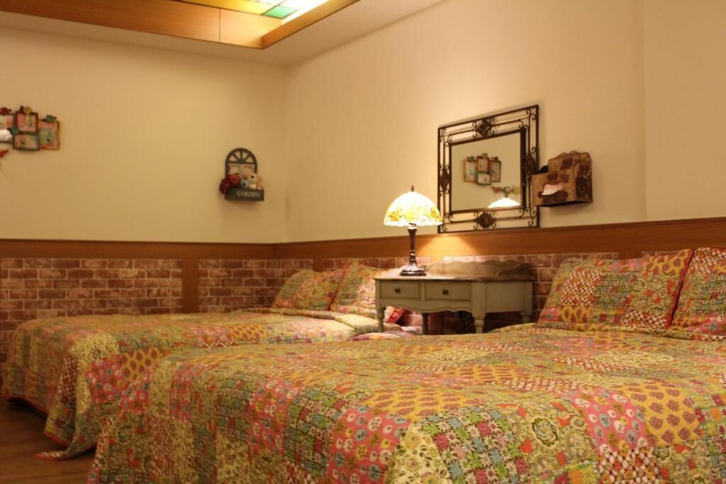 A room with two beds, a nightstand, a lamp, a mirror, and a brick wall.