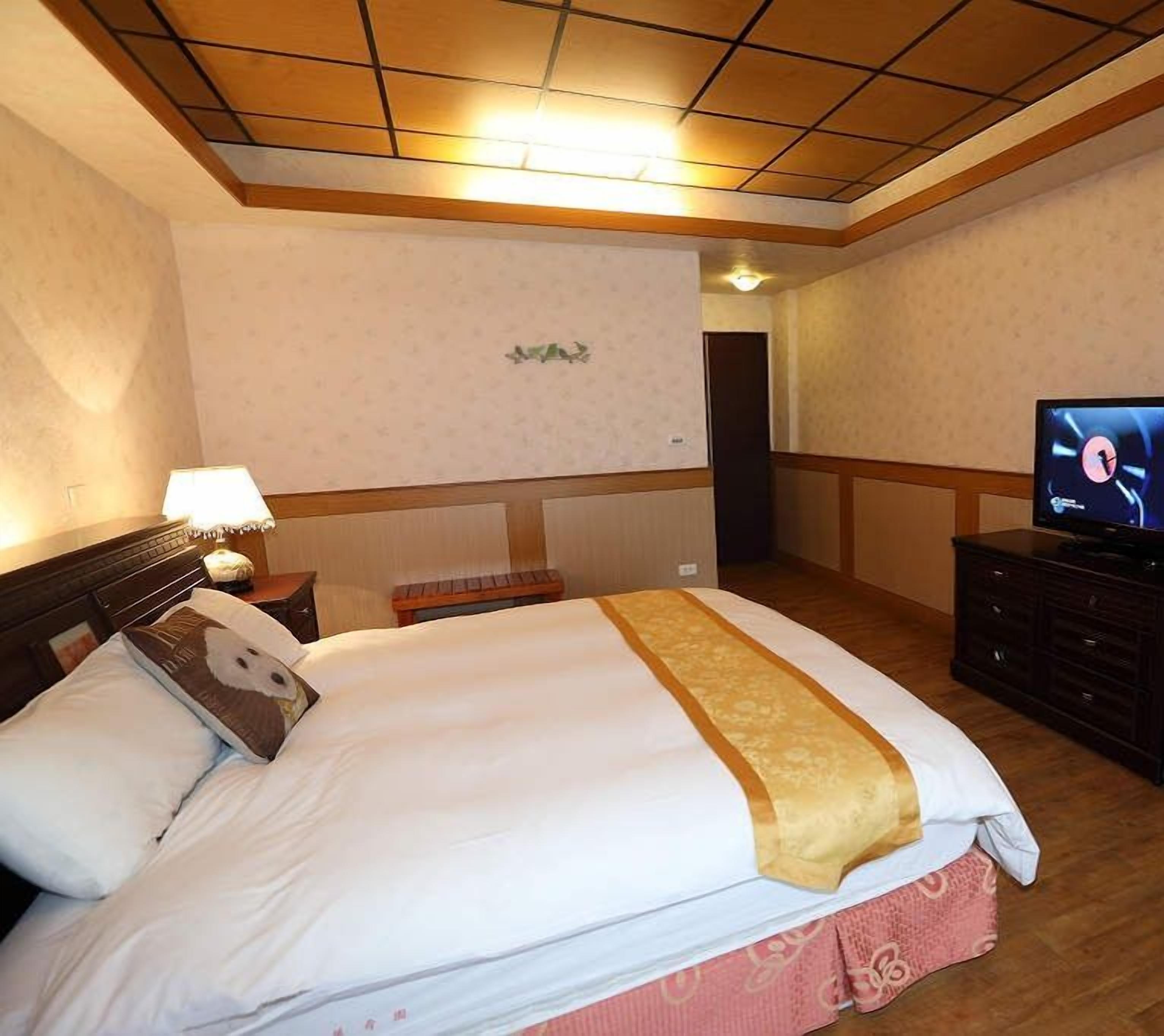 Una habitación de hotel con una cama grande, un televisor, una mesita de noche y una lámpara.