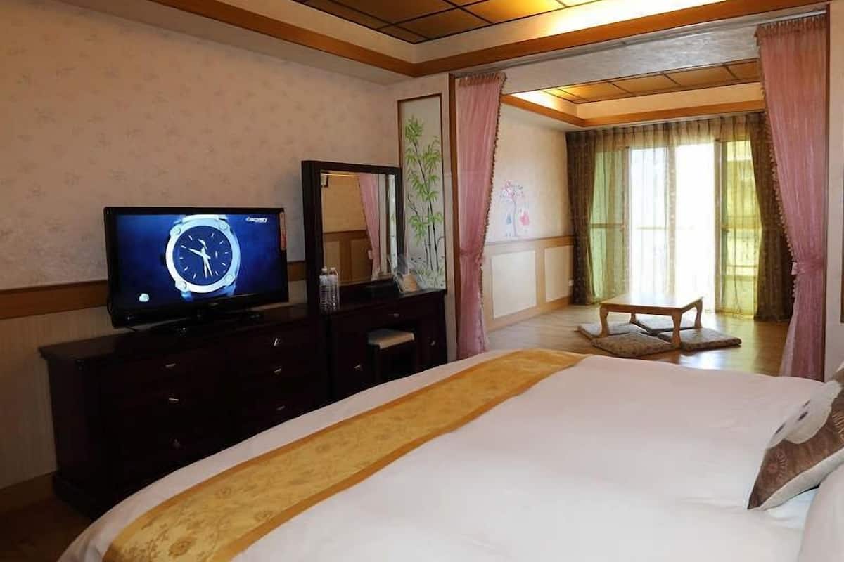 A hotel room with a bed, a television, a dresser, a mirror, and a window with curtains.