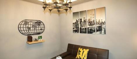 A modern living room with a brown leather sofa, a glass coffee table with water bottles, a world map artwork, and a cityscape wall art.