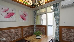 A room with a brick wall, a wooden table with a plant, and two paintings of pink flowers. - First Place B&B - Hualien Railway Station (Hualien City)