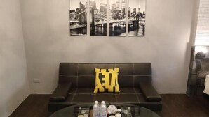 A modern room with a ceiling light fixture, a cityscape artwork, a sofa with a yellow pillow, and a colorful rug. - First Place B&B - Hualien Railway Station (Hualien City)