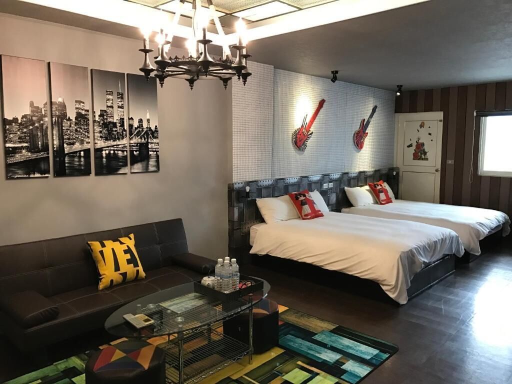 A modern hotel room with a large bed, a sofa, a glass coffee table, and a cityscape mural on the wall.