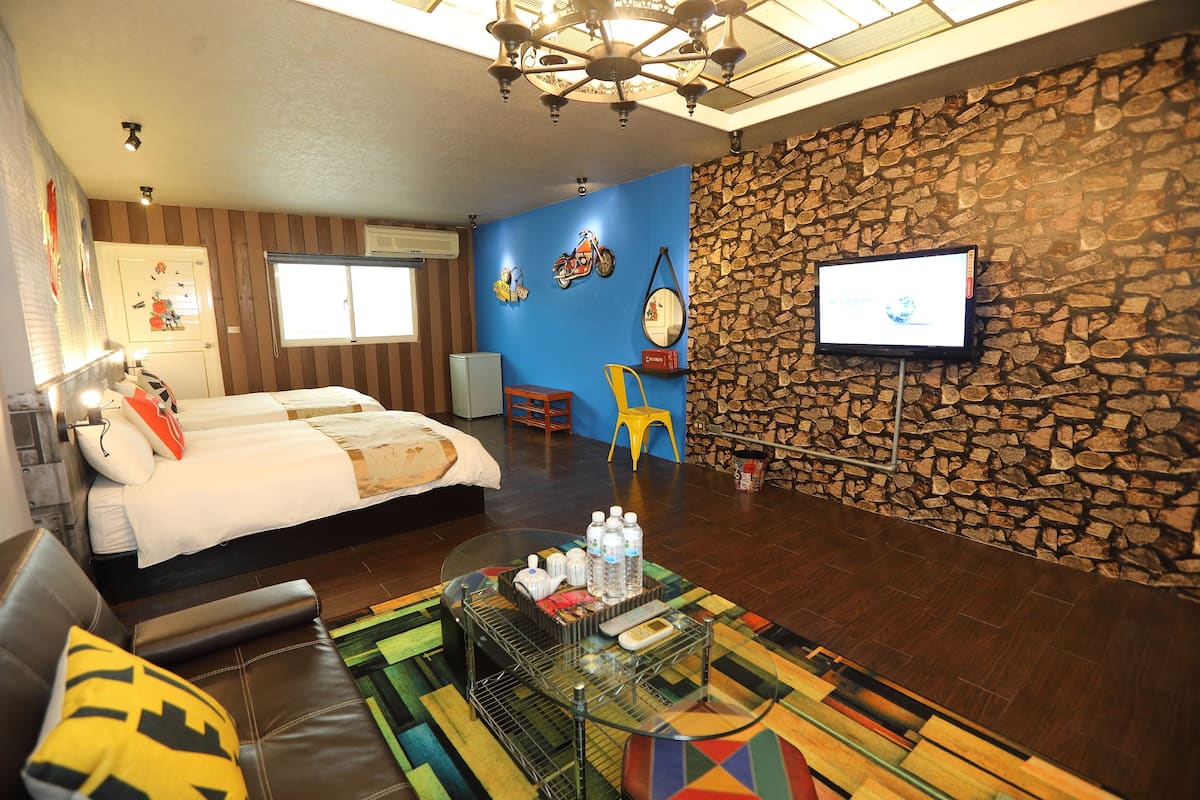 A hotel room with a bed, a sofa, a TV, a stone wall, and a ceiling fan.