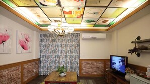 A cozy living room with a wooden table, floral cushions, a television, and a ceiling with a grid pattern. - First Place B&B - Hualien Railway Station (Hualien City)