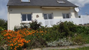 A two-story house with a white picket fence, a satellite dish, and a small garden with orange flowers. - Holiday house with sea view in Hanvec, quiet - 5 people. (Hanvec)