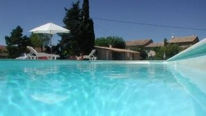 A clear swimming pool with lounge chairs and umbrellas, surrounded by buildings and trees. - Provencal farmhouse with pool  (Joucas)