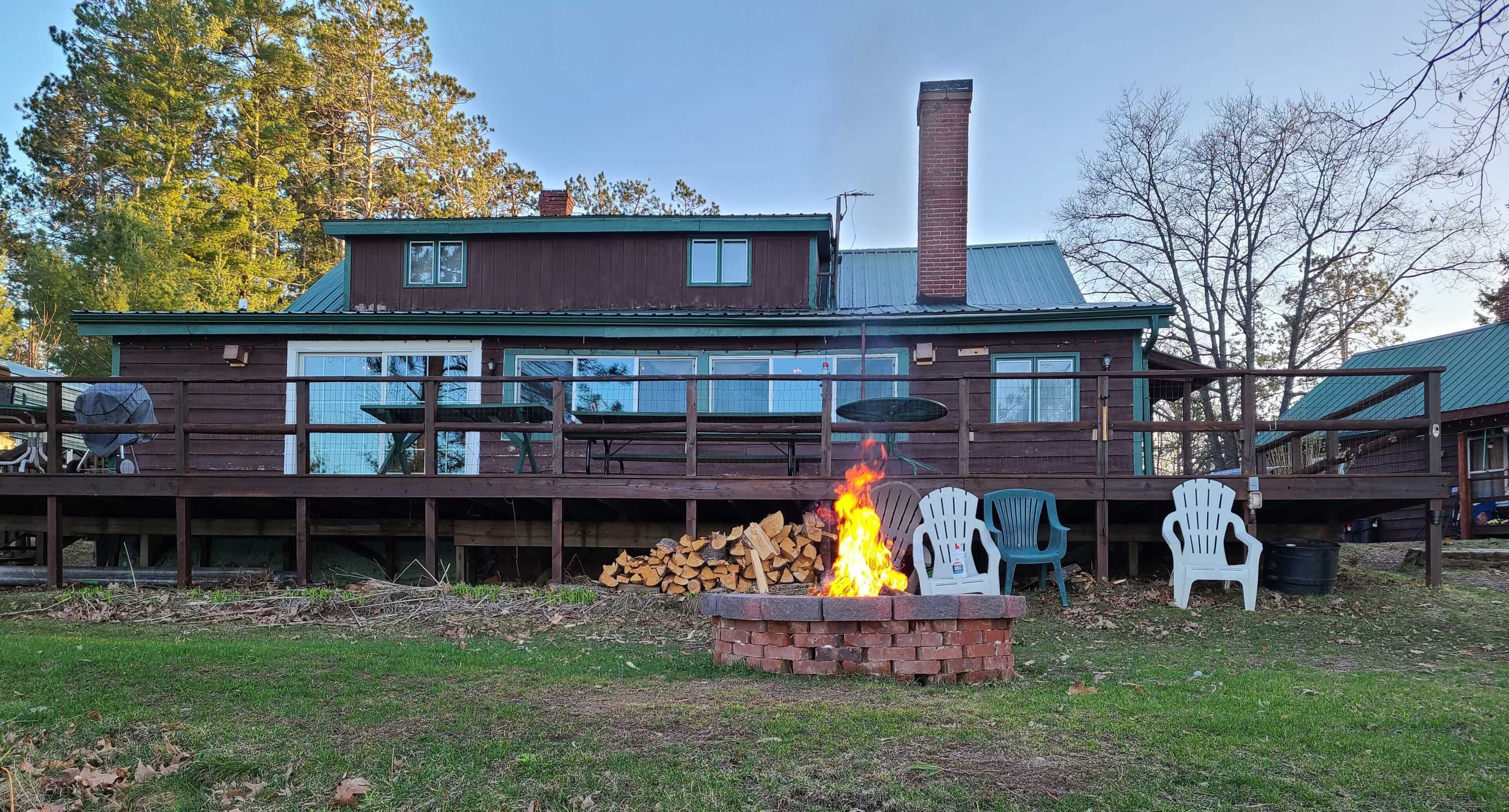 Ein zweistöckiges Holzhaus mit einer Terrasse, einer Feuerstelle und Gartenstühlen.