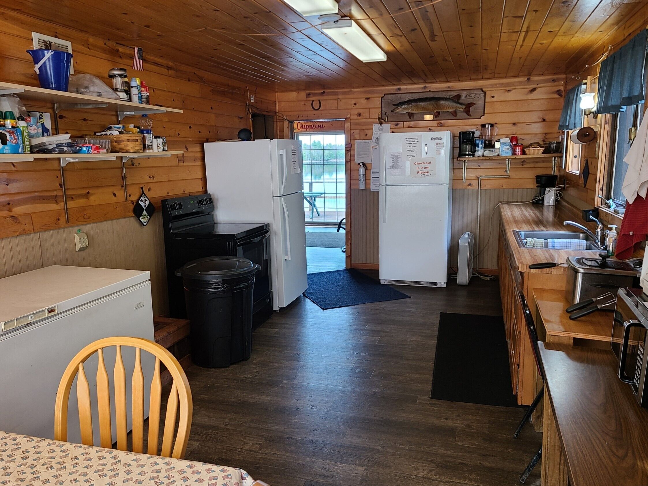 A compact kitchen with wooden walls, a refrigerator, a stove, and a sink.