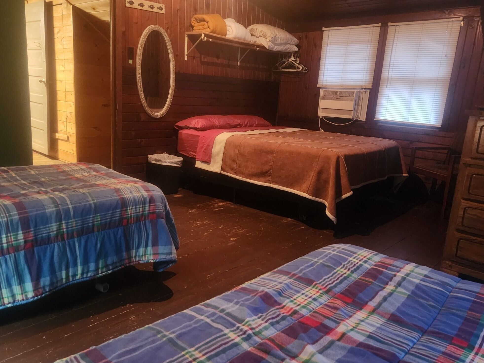 Ein blockhauskamin-Zimmer mit zwei Betten, Holzboden, Spiegel, Heizung und einem Fenster mit Jalousien.