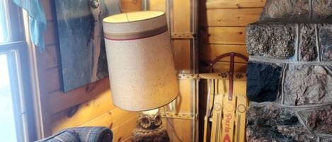 Un interior de cabaña acogedor con un sillón de cuadros, una lámpara, una pared de madera y una chimenea de piedra.