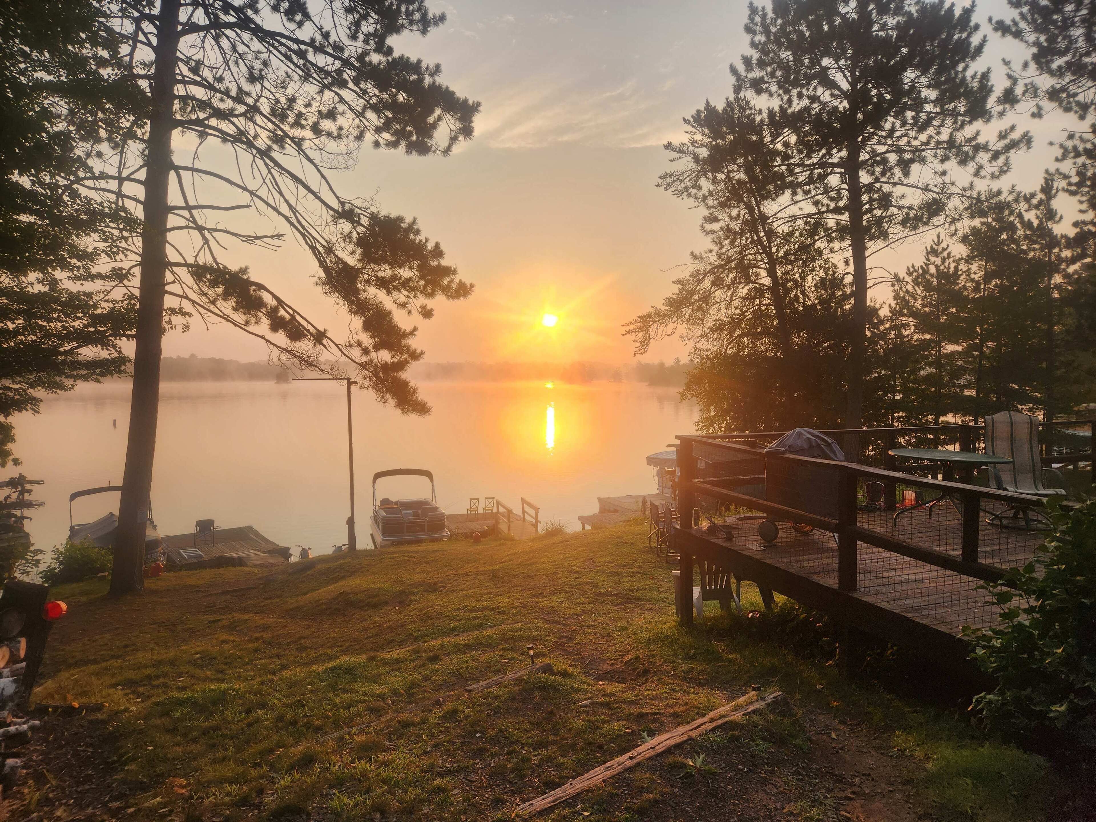 A lakeside deck with a view of the sunset over the water, surrounded by trees.