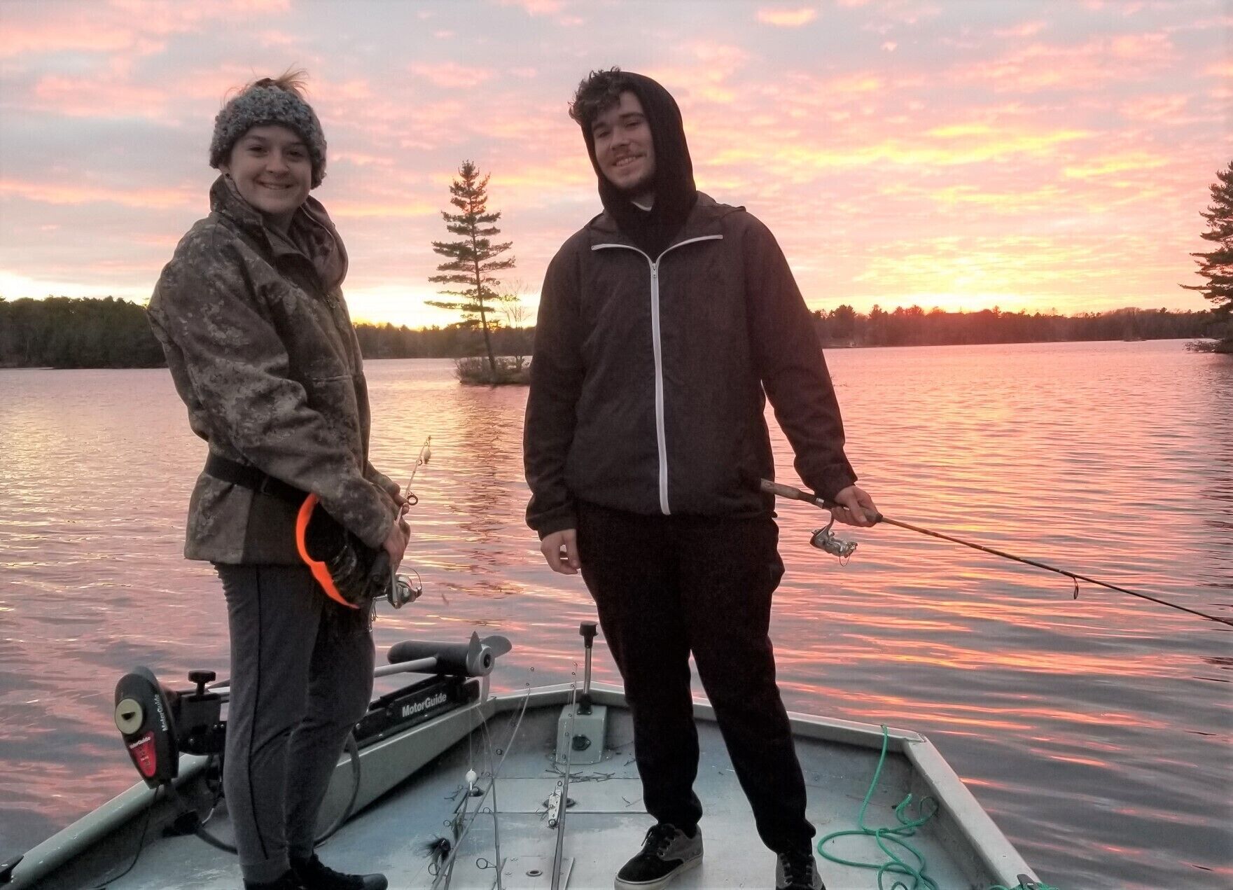 Two people on a boat with fishing rods, a motor guide, and a rope.