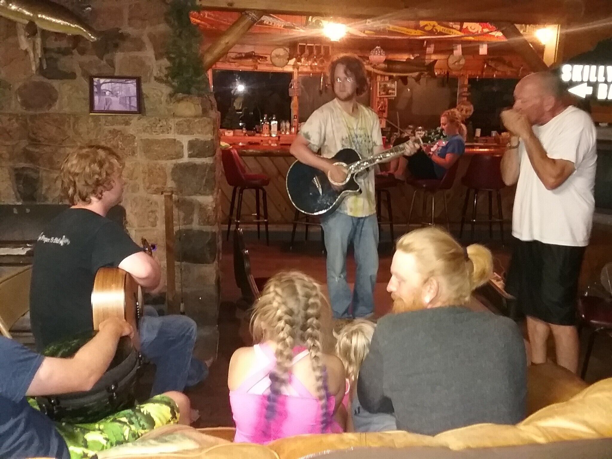 A group of people in a cozy indoor setting with a stone wall and a bar area in the background.