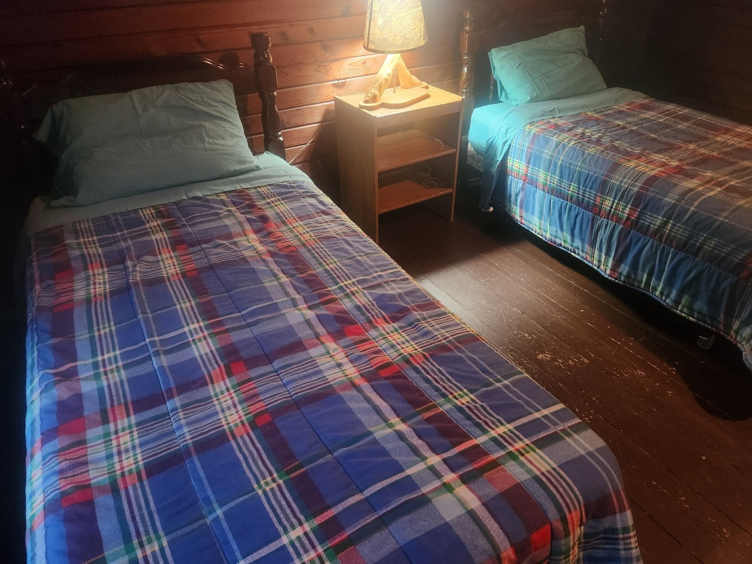 Una habitación con dos camas, cada una con una manta escocesa, un cabecero de madera y una mesita de noche con una lámpara.