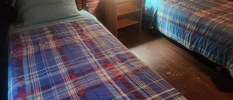 A room with two beds, each with a plaid blanket, a wooden headboard, and a nightstand with a lamp.
