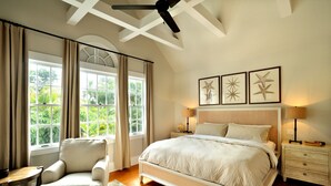 A bedroom with a large bed, two bedside tables, a chair, and a window with curtains.