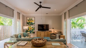 A spacious living room with a ceiling fan, a large flat-screen TV, and a comfortable seating area with sofas and a coffee table.