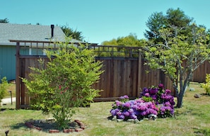 Une clôture en bois, un petit arbre et un parterre de fleurs aux fleurs violettes, le tout dans un jardin arrière.