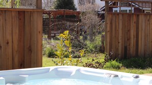 Un bain à remous dans un jardin, avec une clôture en bois et un espace végétal.