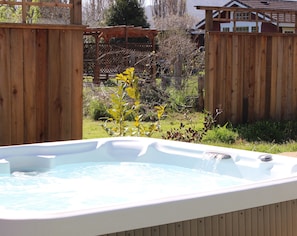 Un bain à remous dans un jardin, avec une clôture en bois et un espace végétal.