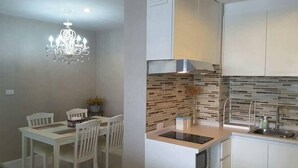 A modern kitchen with white cabinetry, a built-in stove, and a backsplash with a mosaic tile design. - The Energy Condo By AP (Cha-am)