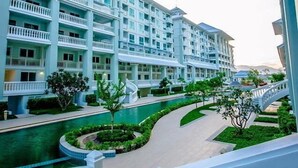 A multi-story hotel with balconies, a swimming pool, and a landscaped garden. - The Energy Condo By AP (Cha-am)