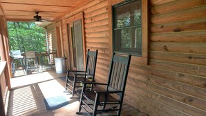 Eine Veranda eines Holzchalets mit zwei Schaukelstühlen, einem Deckenventilator und Blick auf den Wald.