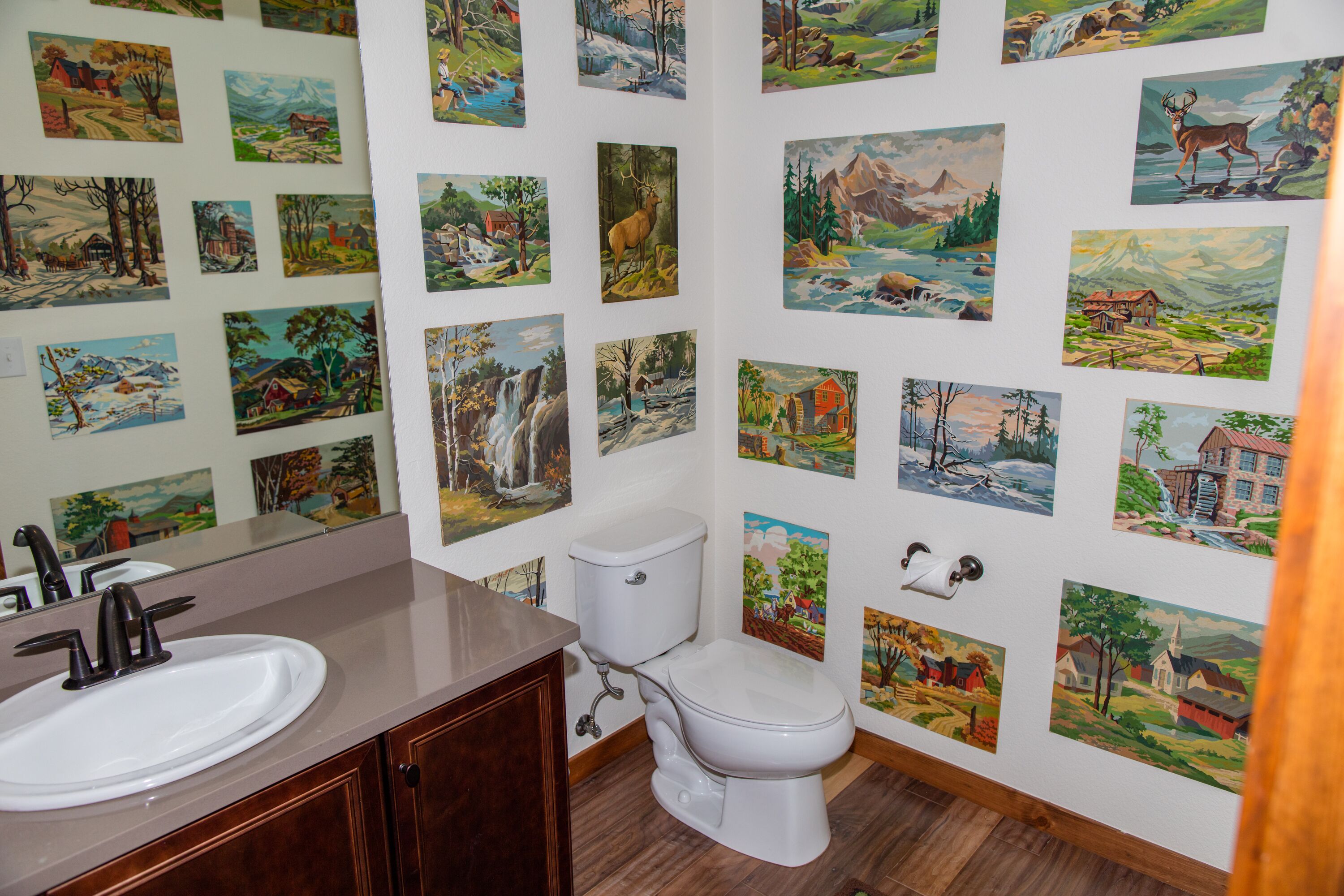 A bathroom with a sink, toilet, and a wall decorated with various landscape paintings.