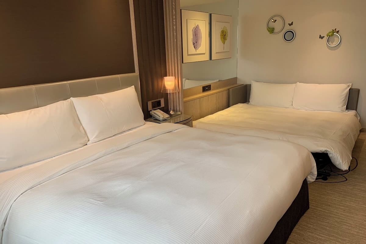 A hotel room with two beds, a bedside table with a lamp, a phone, and wall art.