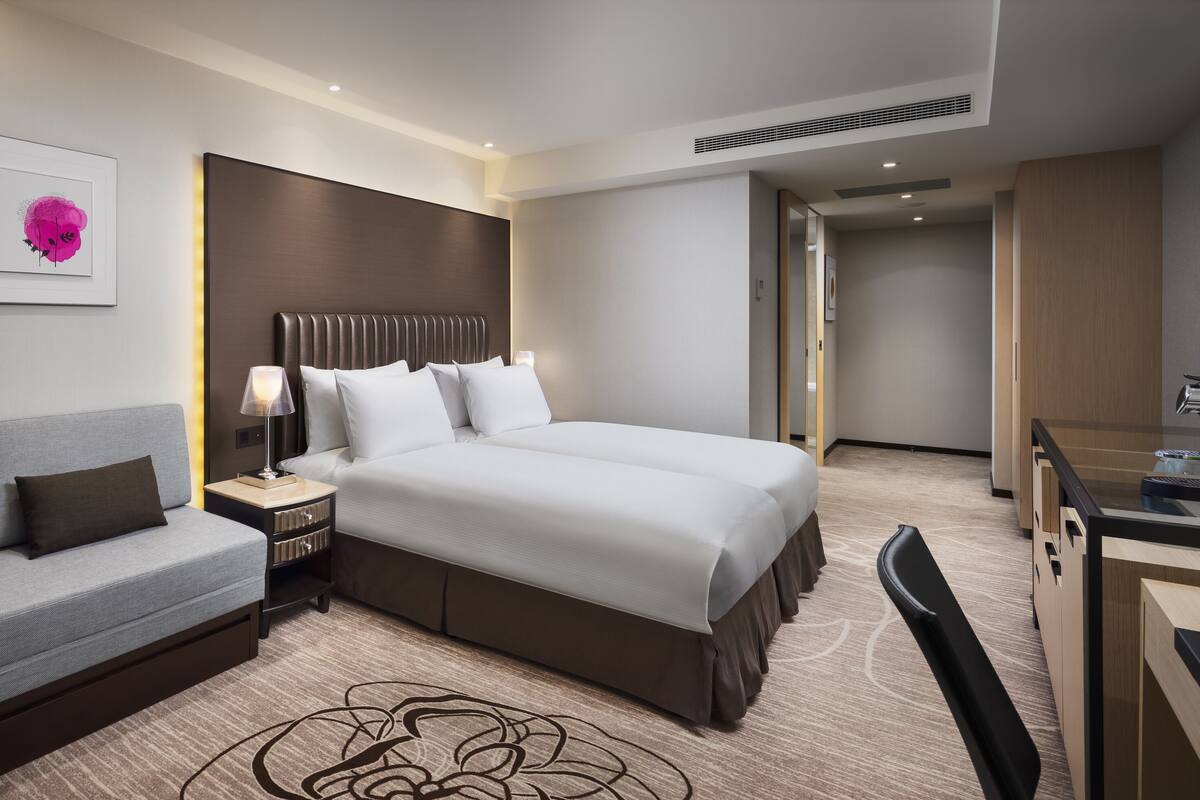 A modern hotel room with a large bed, a sofa, a desk with a coffee machine, and artwork on the walls.