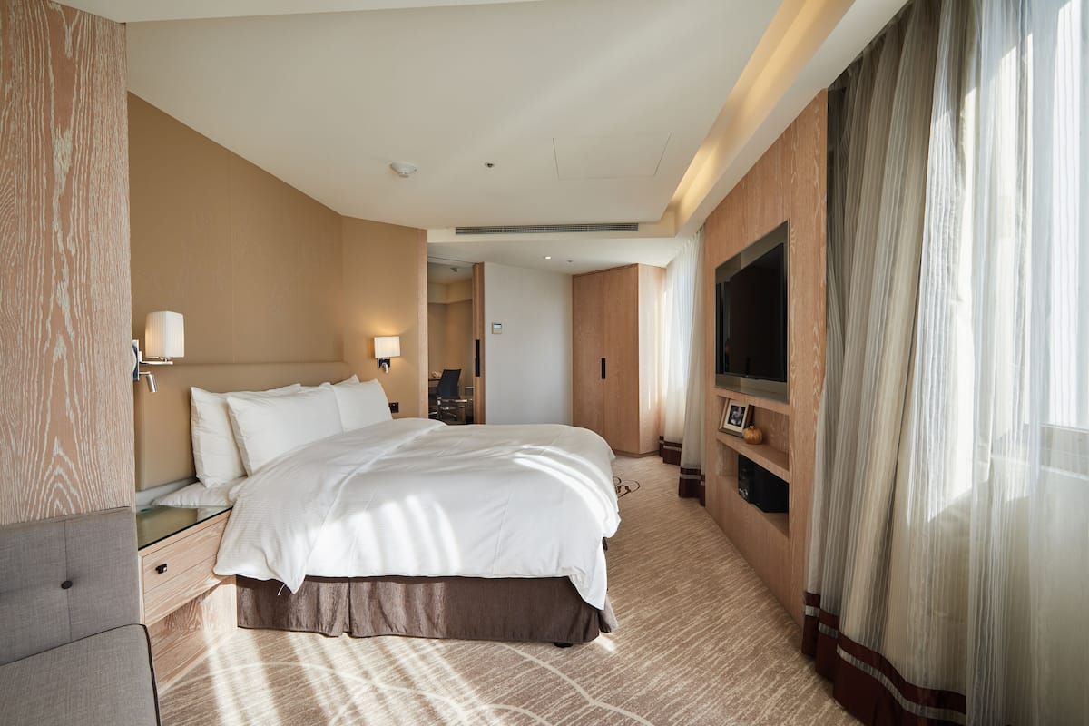 A hotel room with a large bed, bedside tables, a TV, and a view of the outdoors.