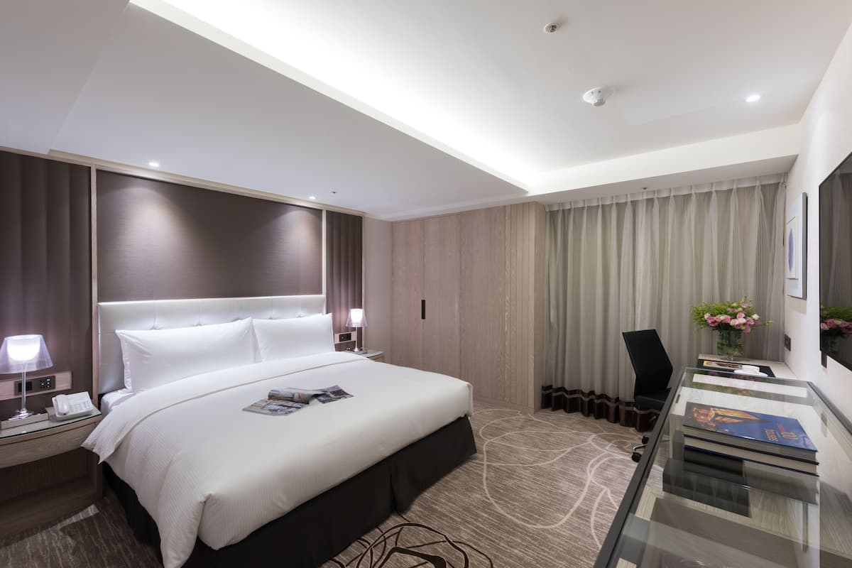 A modern hotel room with a large bed, a desk with a computer, a chair, and a TV.