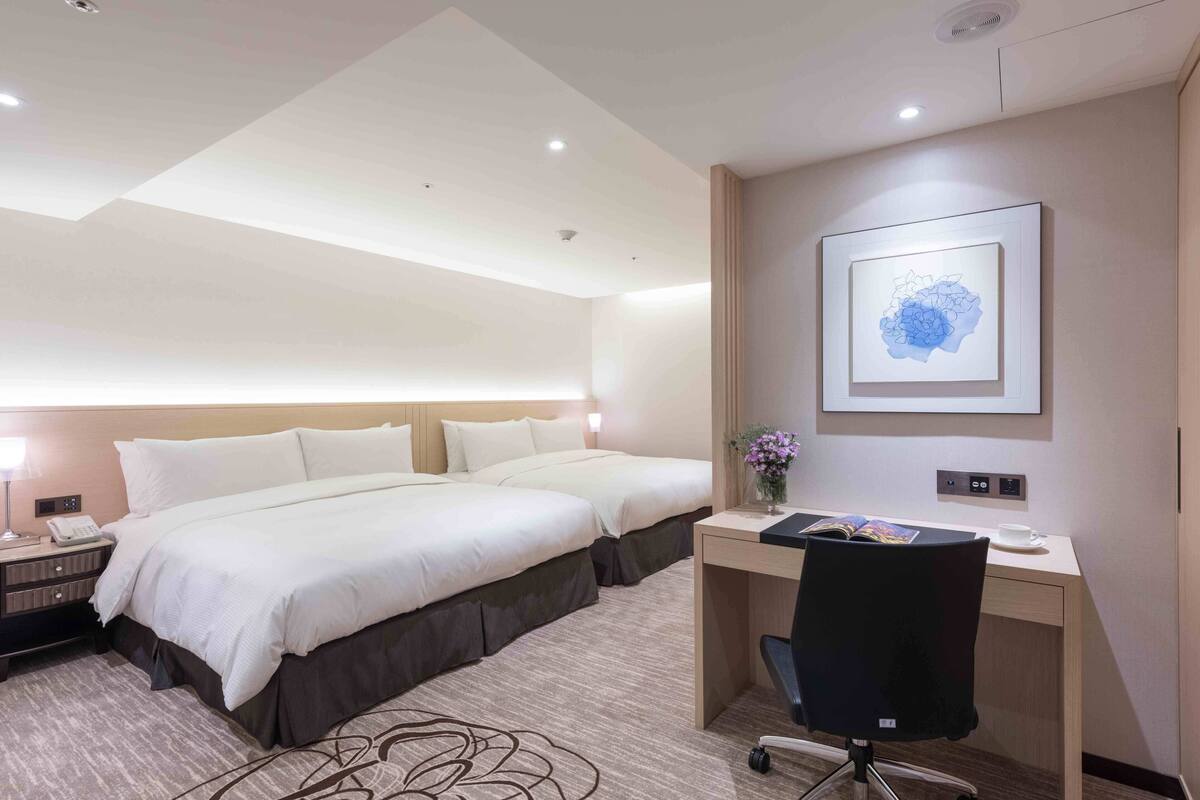A hotel room with two beds, a desk, a chair, a phone, and a framed picture on the wall.