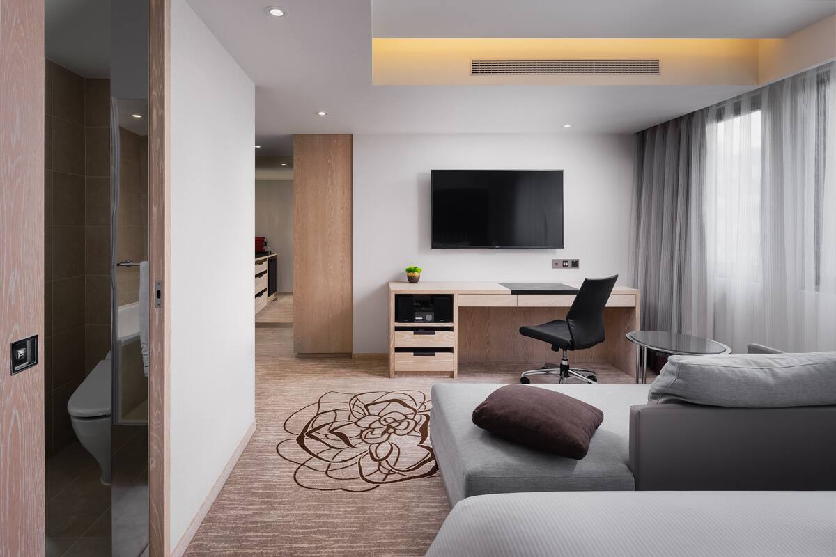 A modern hotel room with a bed, a desk with a chair, a TV, and a small table.