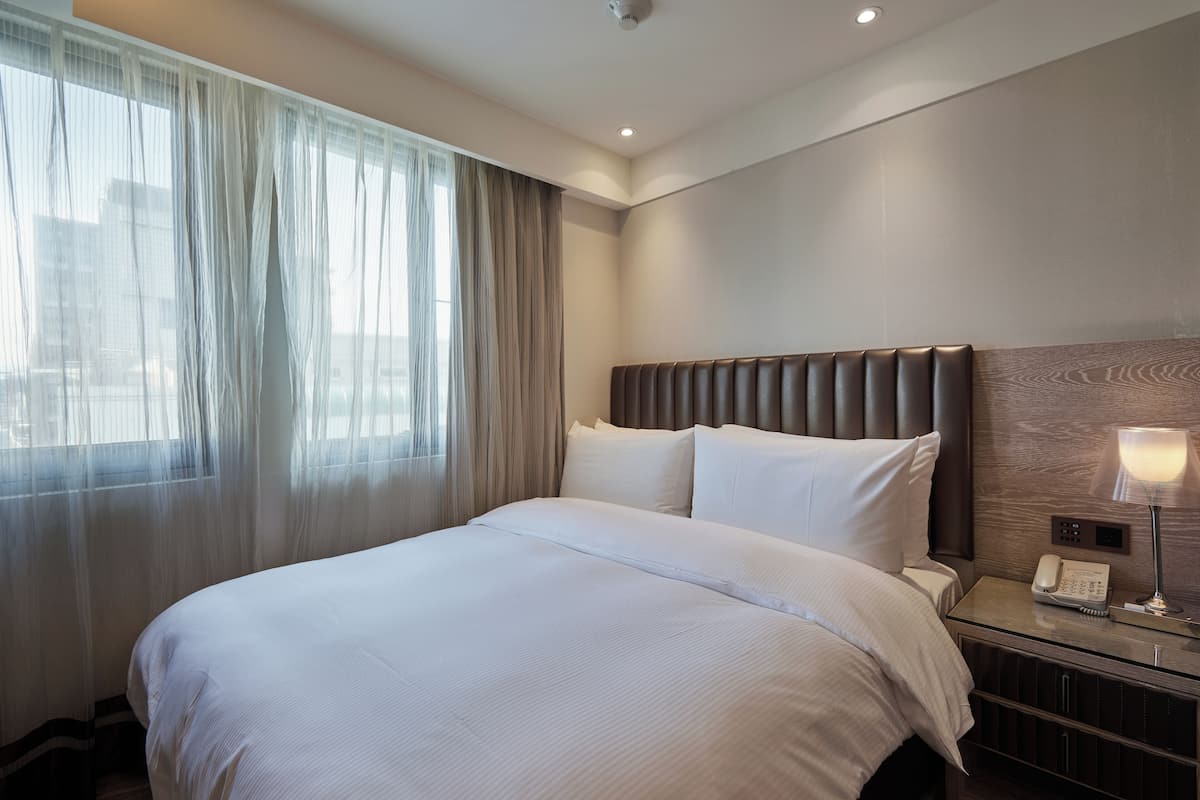A hotel room with a large bed, a bedside telephone, and a nightstand with a lamp.