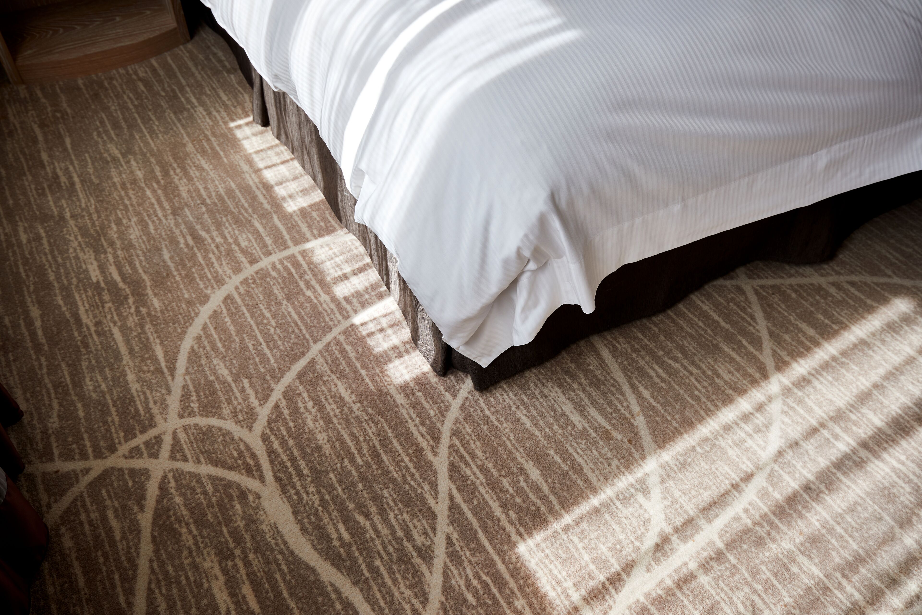 A bed with a white bedspread and a patterned carpet.