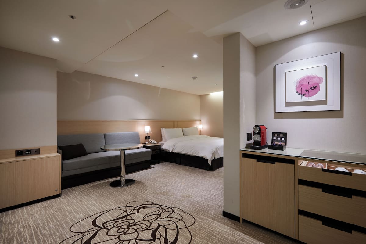 A modern hotel room with a sofa, bed, desk, and a framed artwork on the wall.