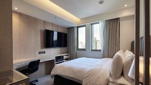 Ein modernes Hotelzimmer mit einem großen Bett, einem Schreibtisch mit Stuhl, einem Flachbildfernseher und Blick auf die Stadt durch die Fenster.