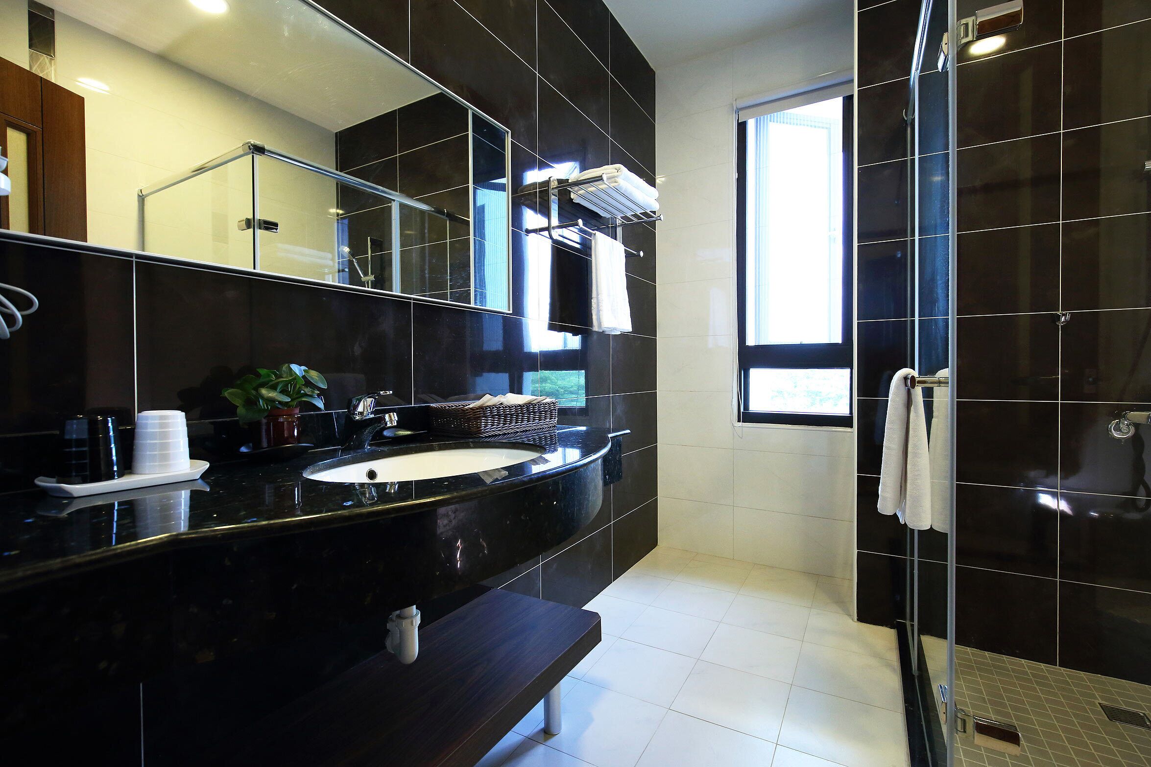 A modern bathroom with a black vanity, a large mirror, a glass shower enclosure, and a window providing natural light.