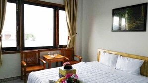 A hotel room with a bed, a small table, two chairs, and a window with curtains. - Bac Nam Motel (Da Nang)