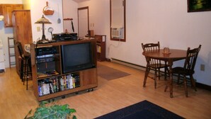 A living room with a wooden entertainment center, a dining table with chairs, a ceiling fan, and a window with blinds. - Small cabin in the woods Peaceful retreat (East Bernstadt)