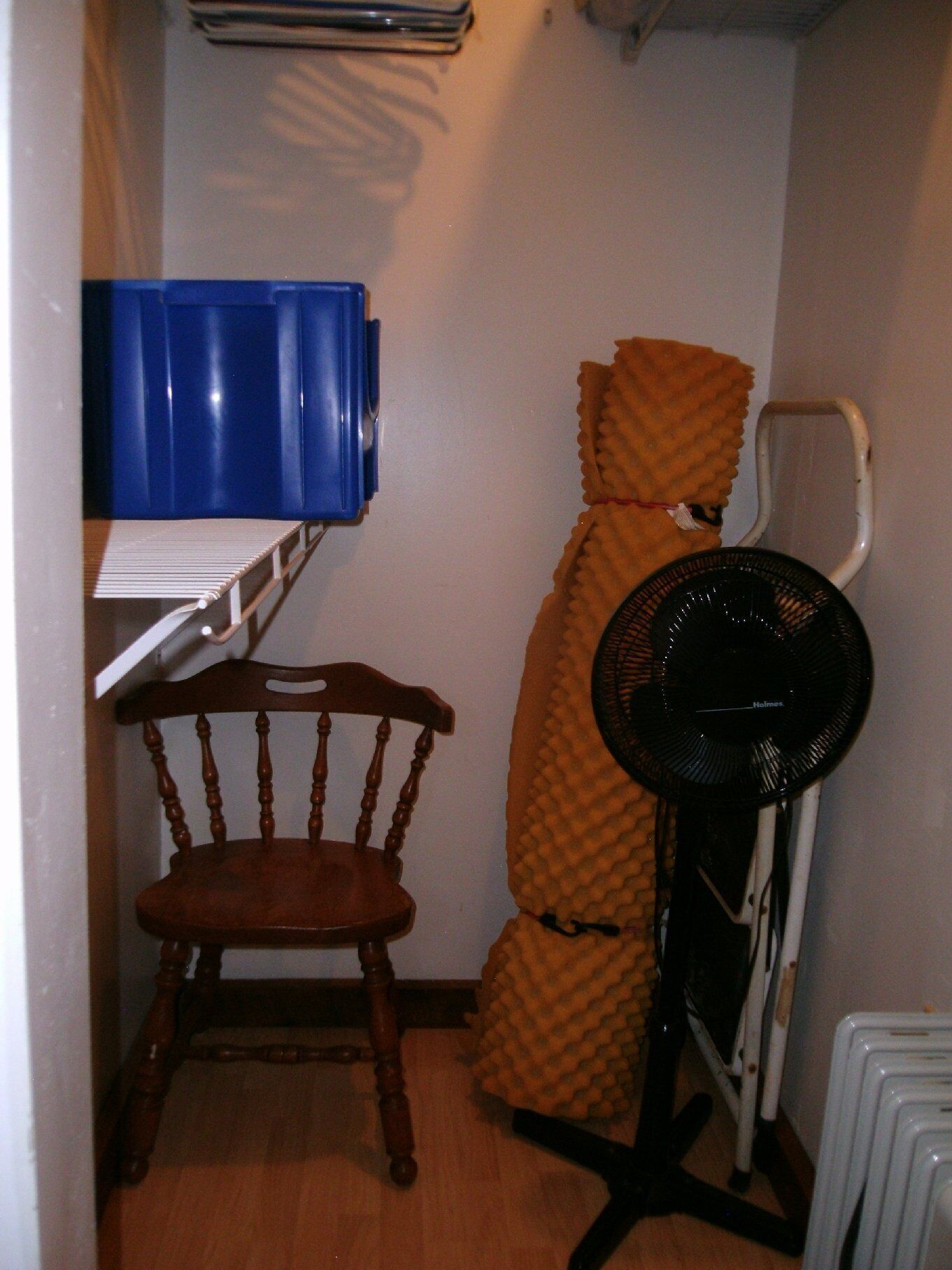 A small room with a wooden chair, a blue storage unit, a heater, and a fan.