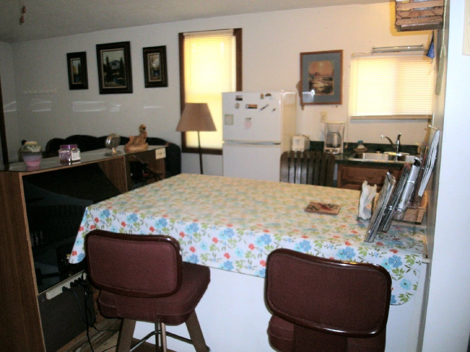 Una cocina compacta con refrigerador, estufa y lavamanos. Hay dos sillas y una mesa con mantel floreado.
