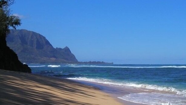 A beach with a mountain in the background and waves crashing onto the shore.